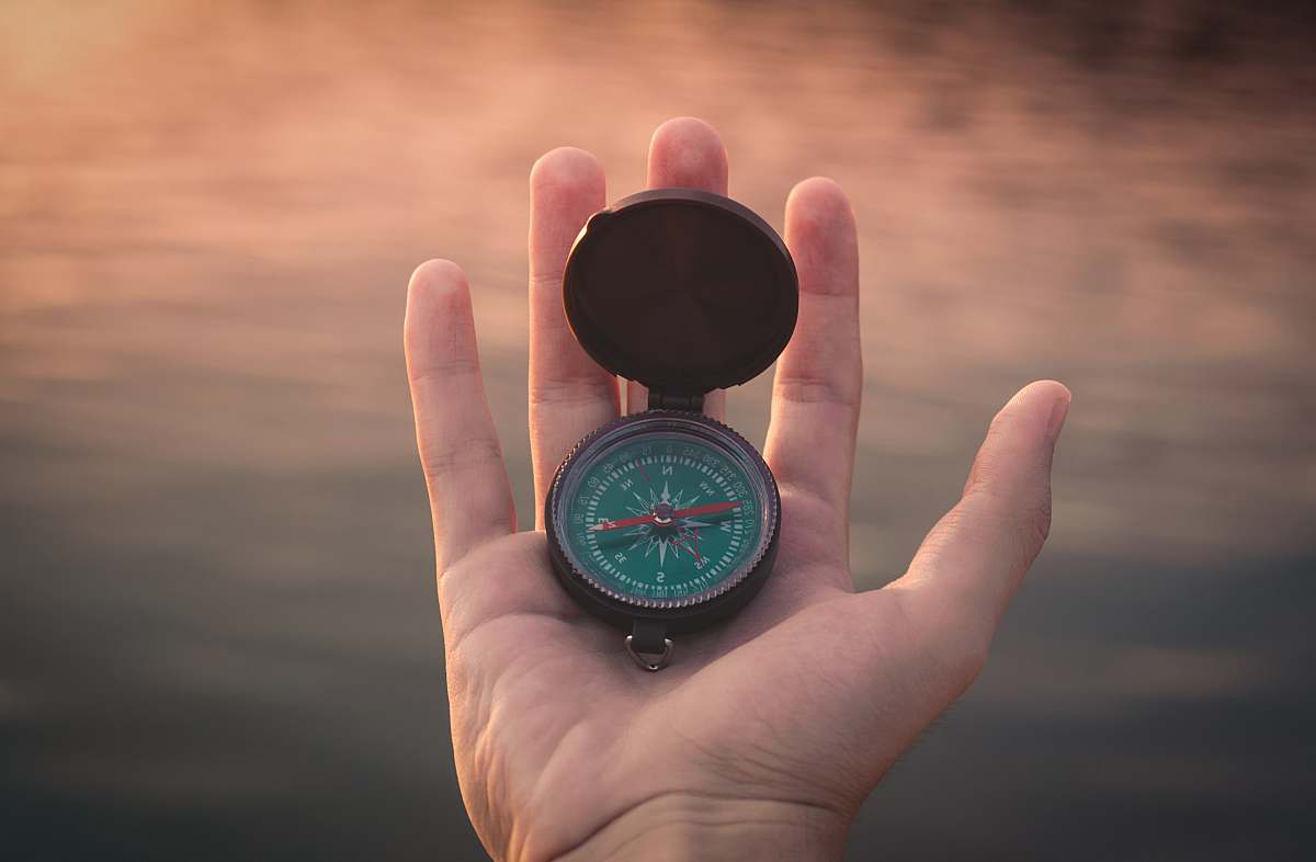 compass person holding black and green compass pointing to west sunset