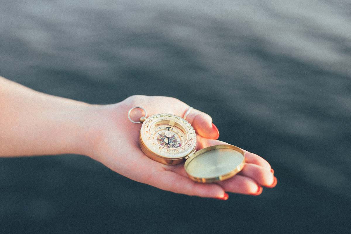 hands person holding gold-colored pocket watch compass