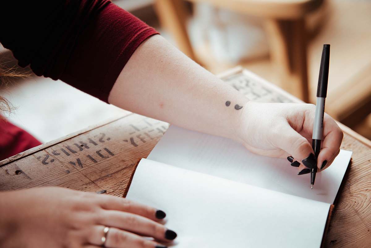 person person holding pen above white open notebook page skin