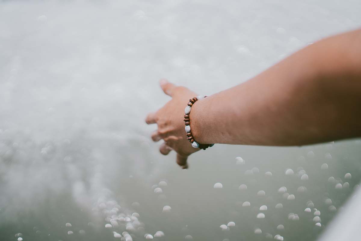 human person wearing beaded brown-and-white bracelet touching splashing water person