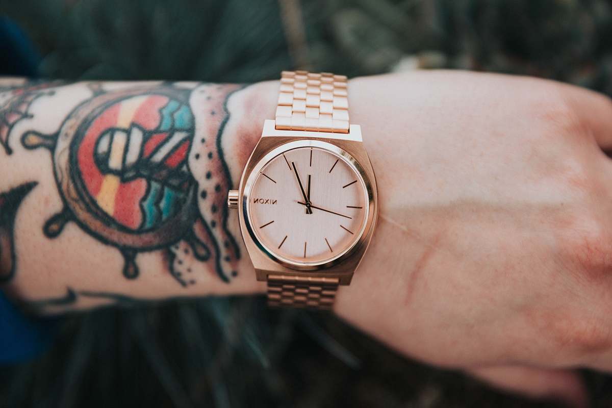 wrist person wearing round gold-colored analog watch display at 12:04 o'clock watch