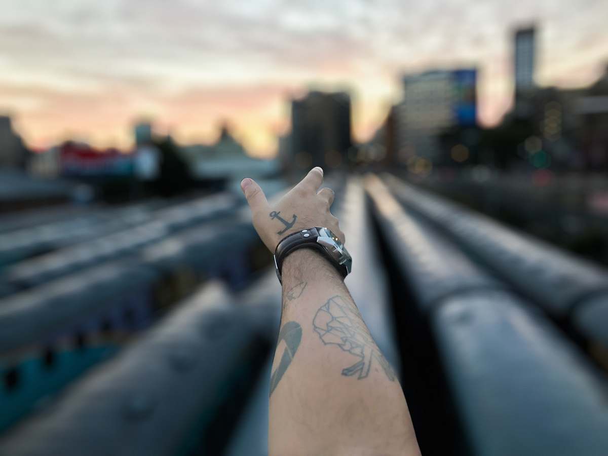tattoo tilt shift photography of man's left hand pointing high-rise building ornament