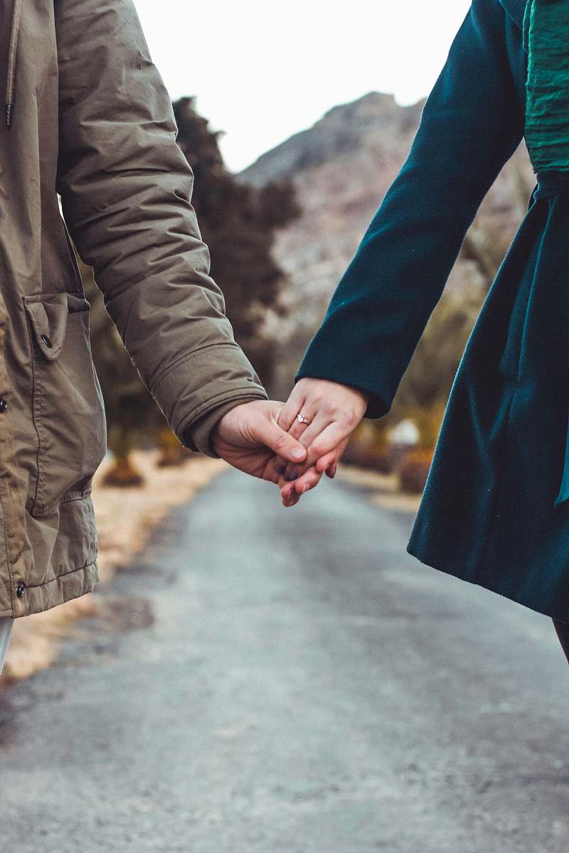 human two person holding hands while walking on asphalt road holding hands