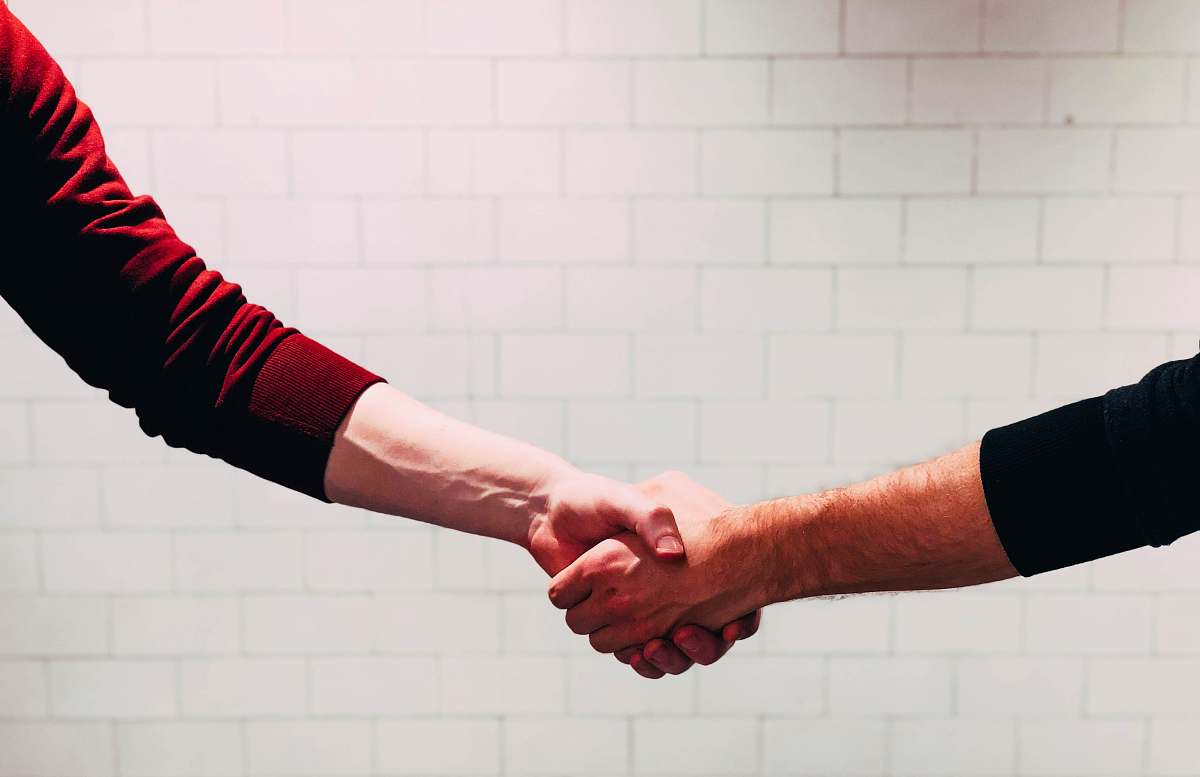 arm two person shaking hands near white painted wall handshake