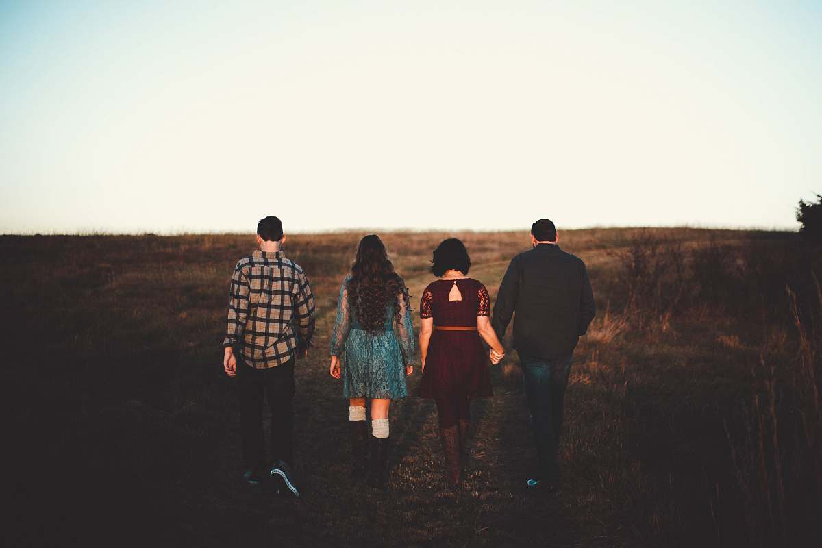 human two women and two men walking at green grass field holding hands