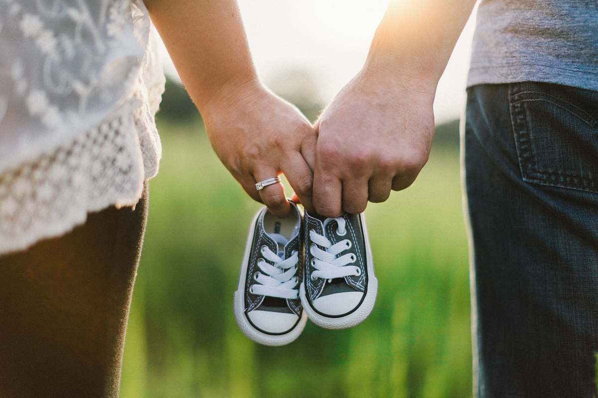 baby woman and man holding black crib shoes standing near green grass during daytime holding hands