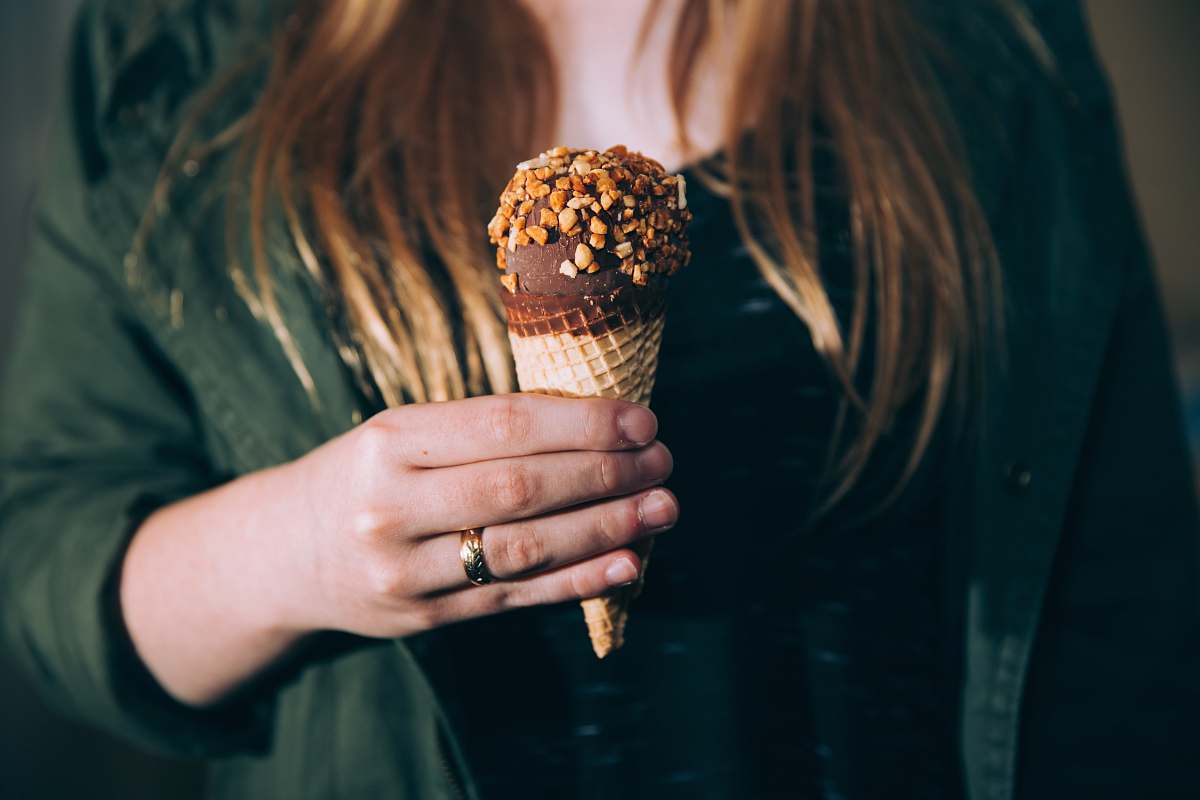 people woman in green jacket holding chocolate ice cream coated of nuts during daytime shallow focus photography food
