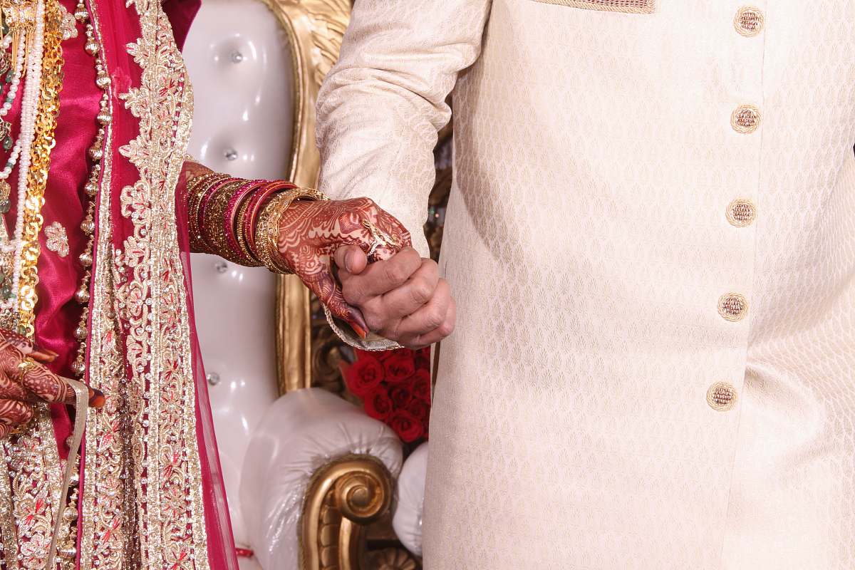 wedding Bride in red and gold dress holds hands with groom in India india