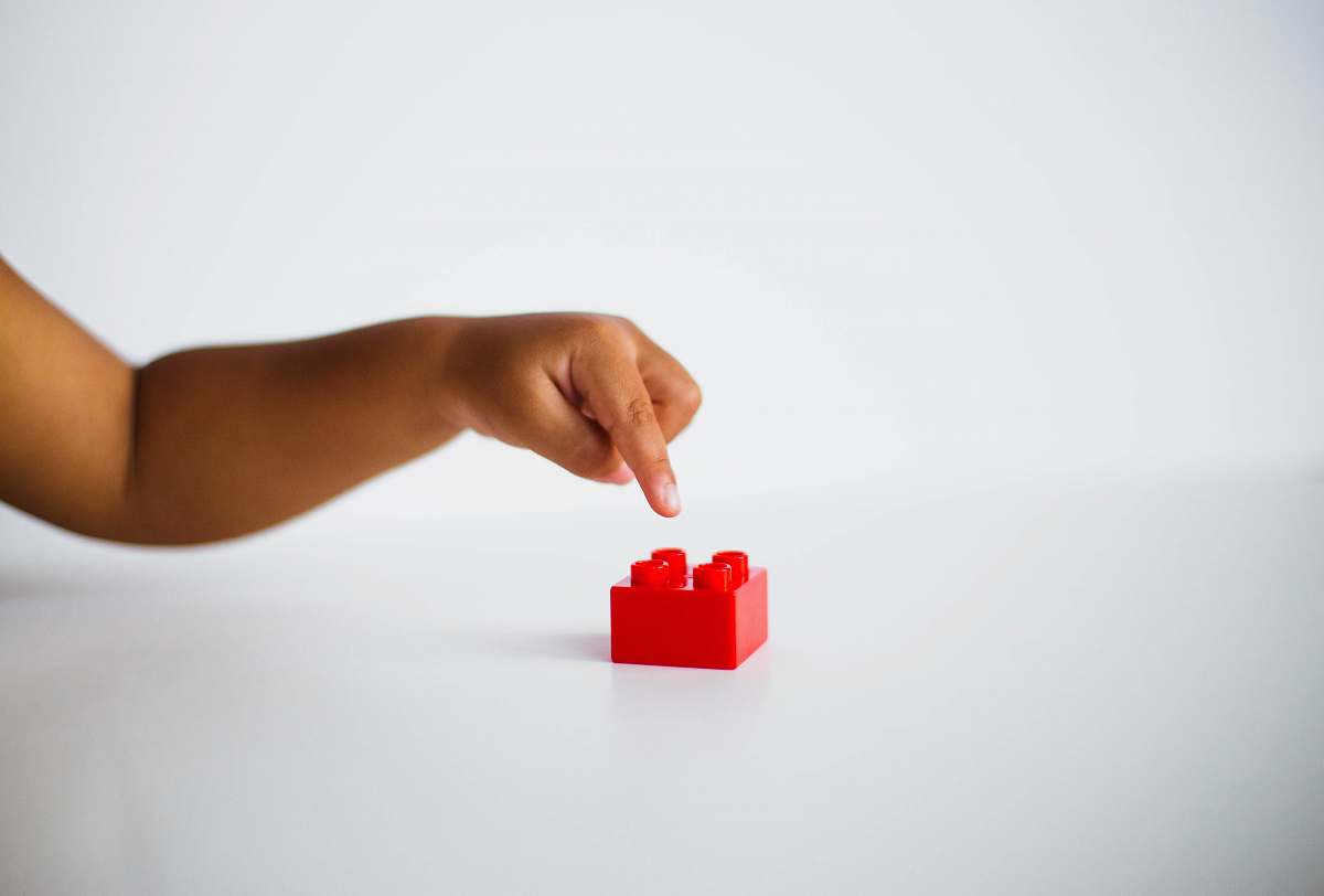 person child pointing to red interlocking brick toy hand