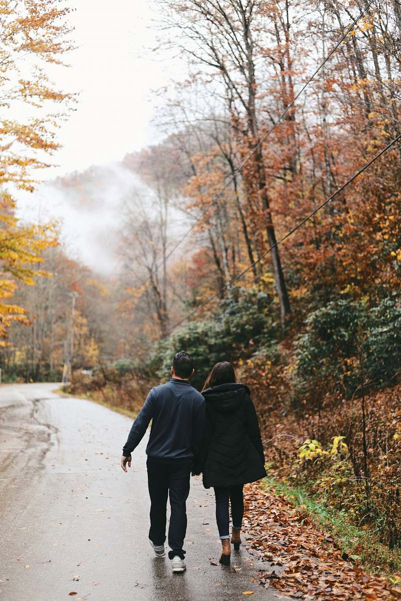 person couple walking at the road between trees walking
