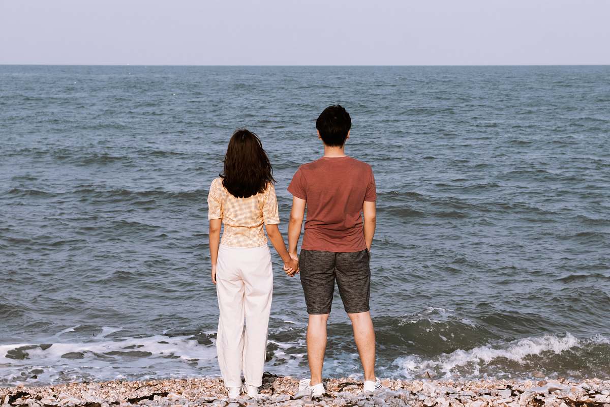 person man and woman standing infront of ocean water at daytime people