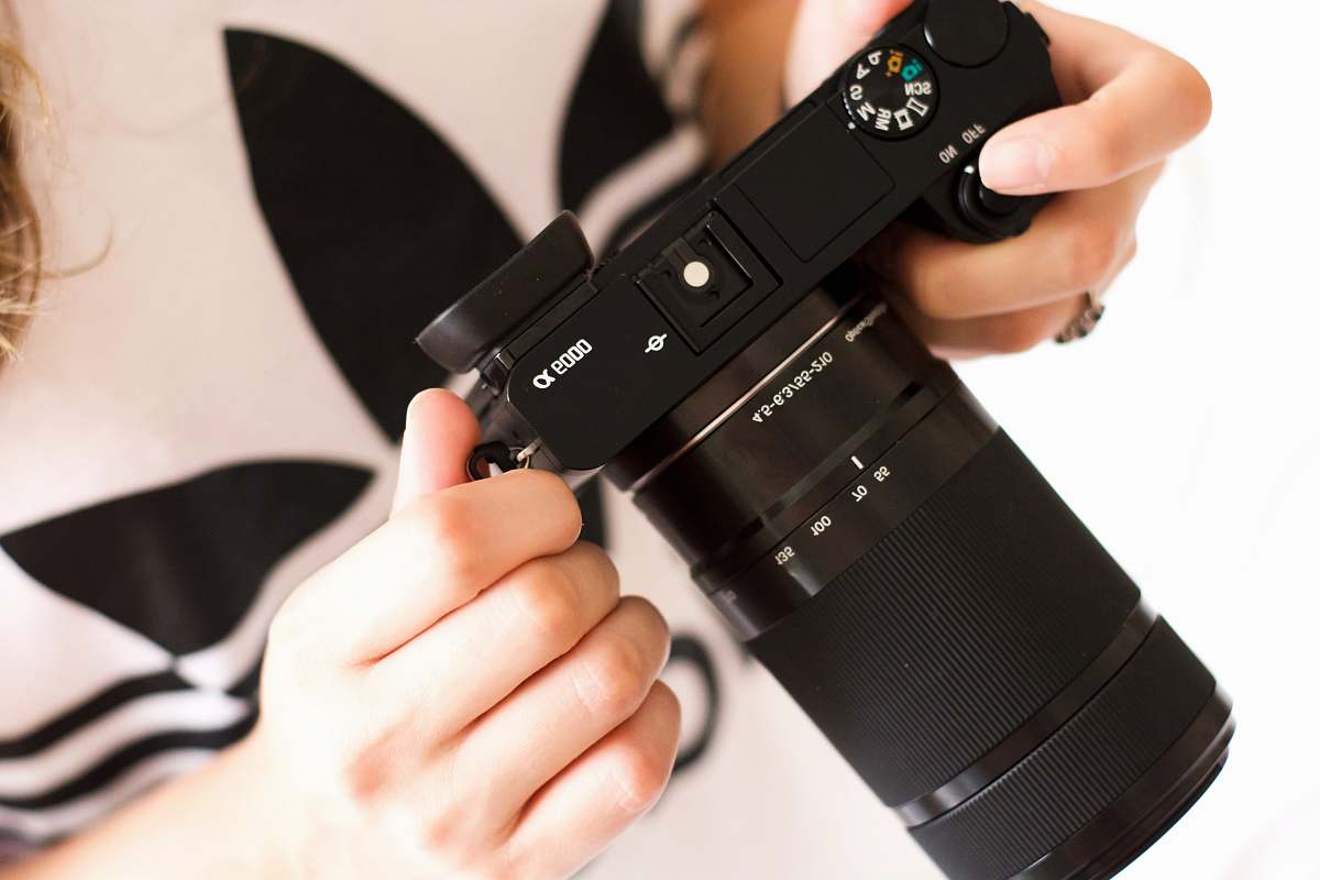 camera person holding black DSLR camera electronics