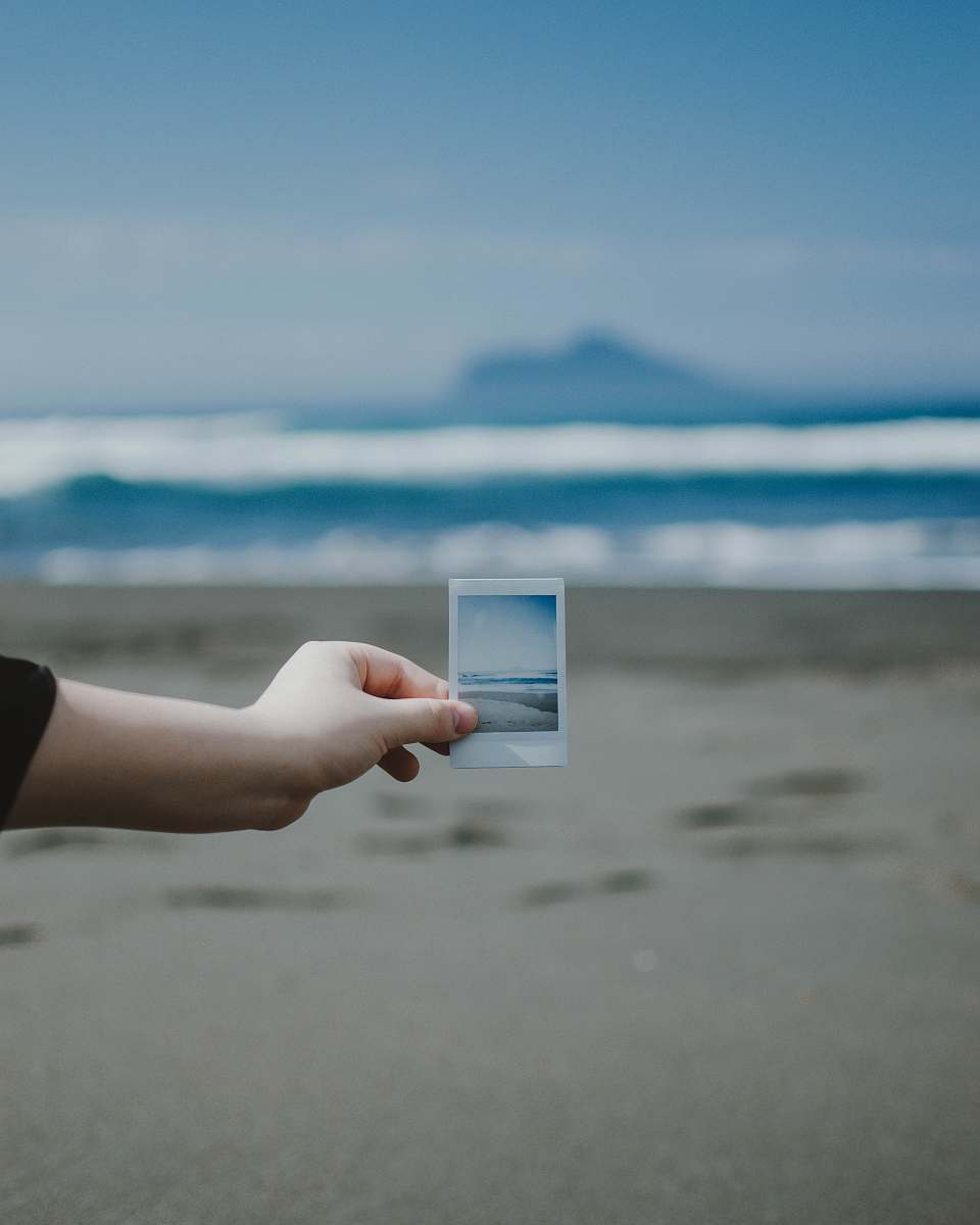 person person holds photo of ocean at the beach finger
