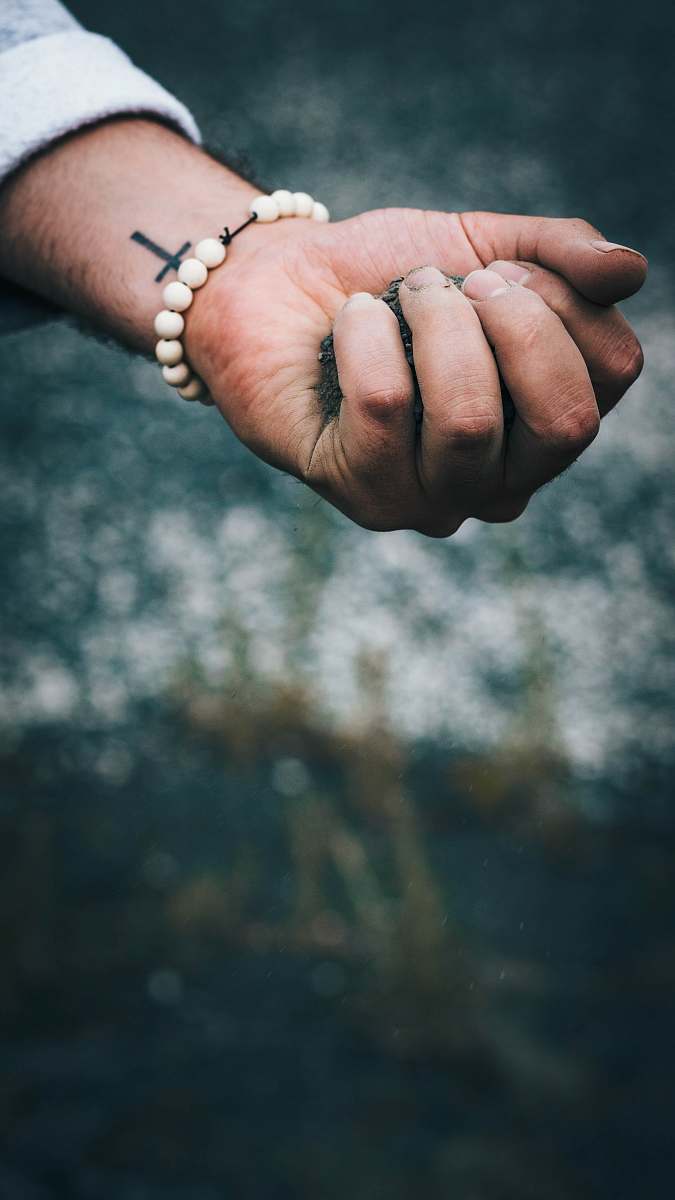 person person wearing beaded white bracelet with dirt in hand hand