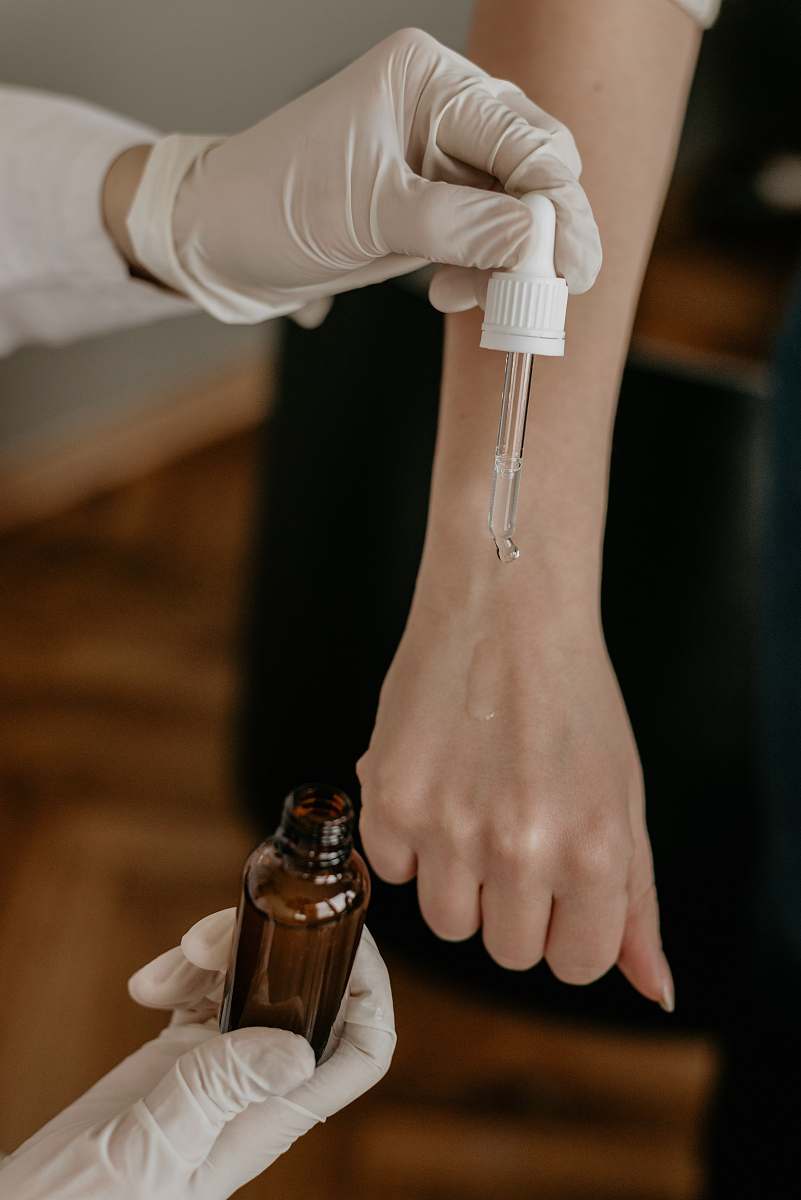 person person with white gloves holding drop bottle pointing on another person's hand test