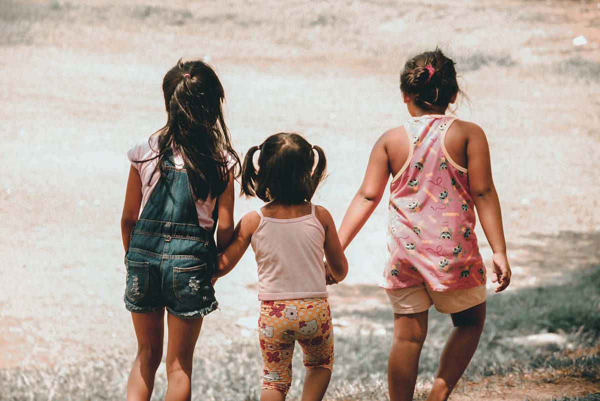 person three girls holding each other hand walking towards brown soil people