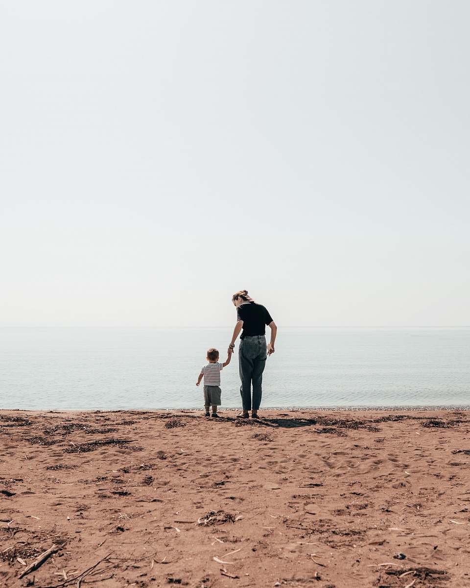 person woman and toddler standing beside seashore during daytime hand