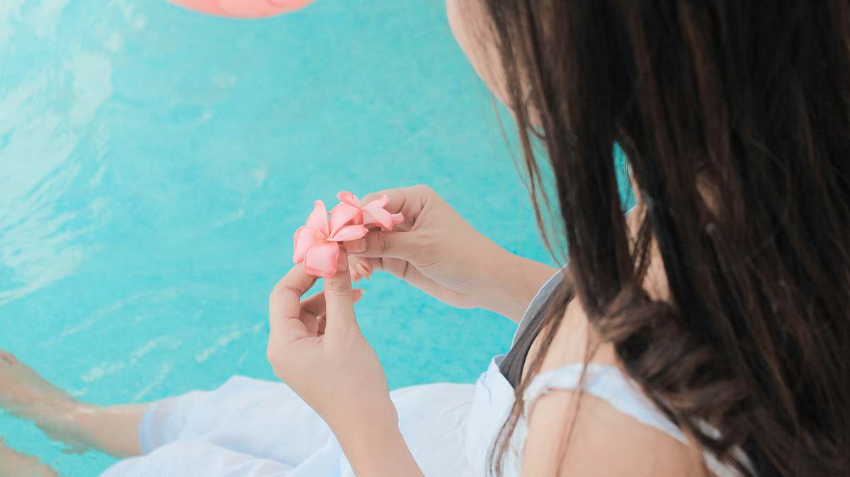 person woman holding pink petaled flower while both feet floats on water hand
