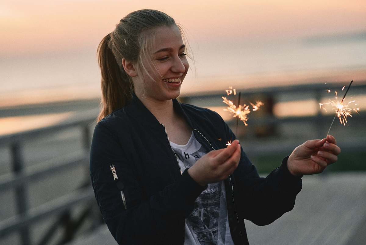person woman wearing black zip-up jacket standing while holding lighted sparklers finger