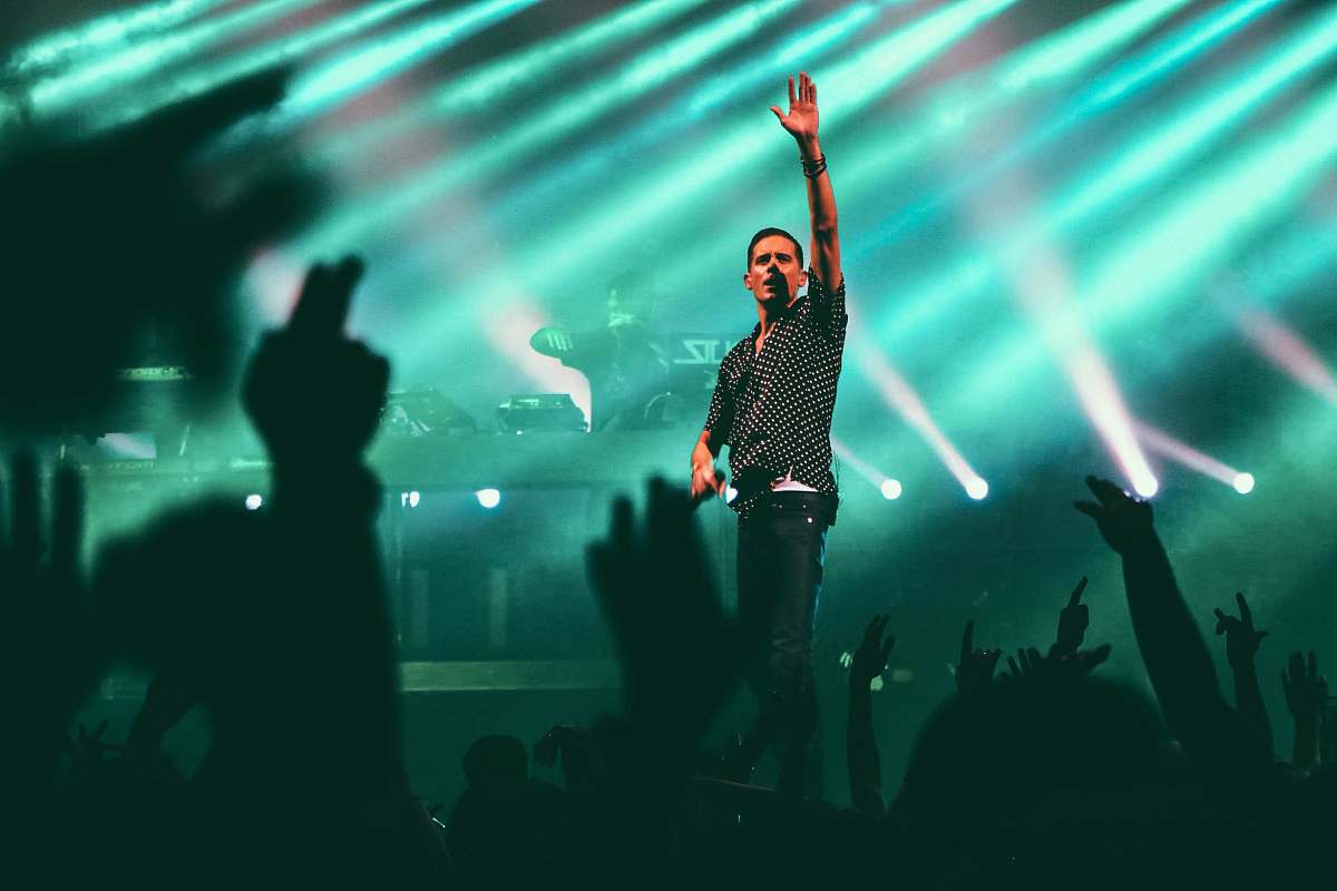 light man in black and gray button-up collared shirt standing on stage with green lights turned on concert