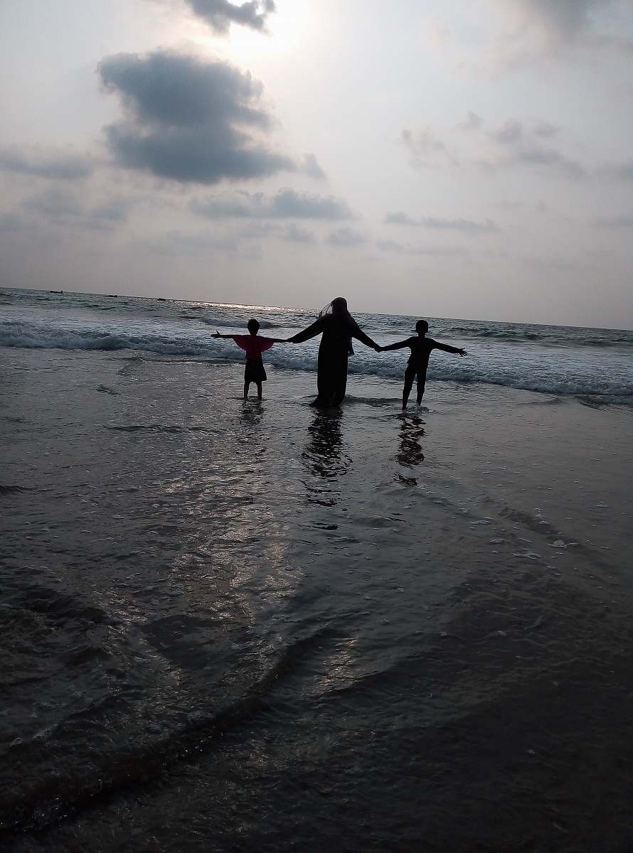 ocean three person standing in front of shoreline outdoors