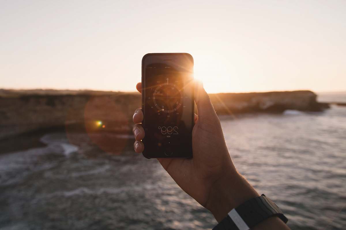 sunlight person holding black phone beside body of water under white sky during golden hour phone