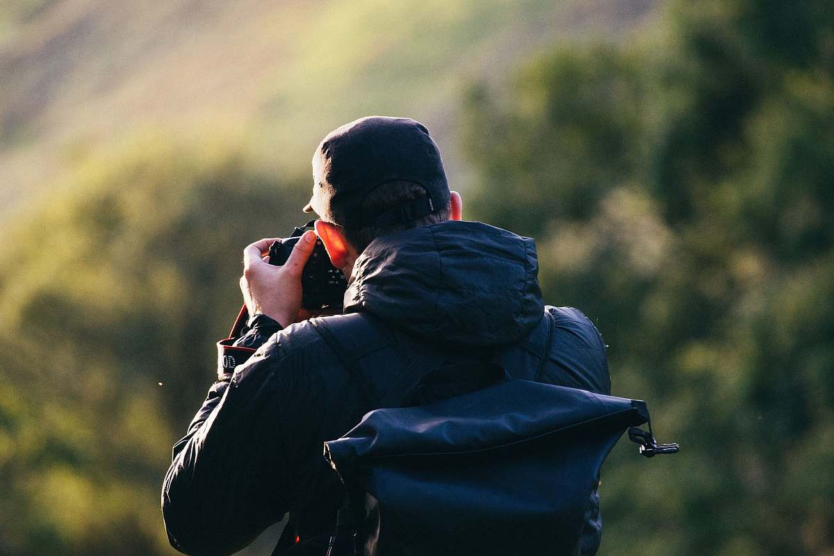 person man standing near mountain cliff while taking photo human