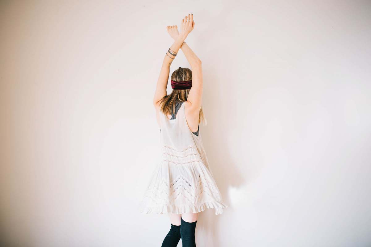 human woman wearing white sleeveless top with hands above head dance