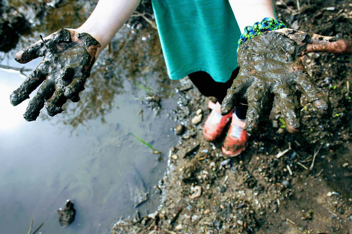 finger child in green top with mud on hand hand
