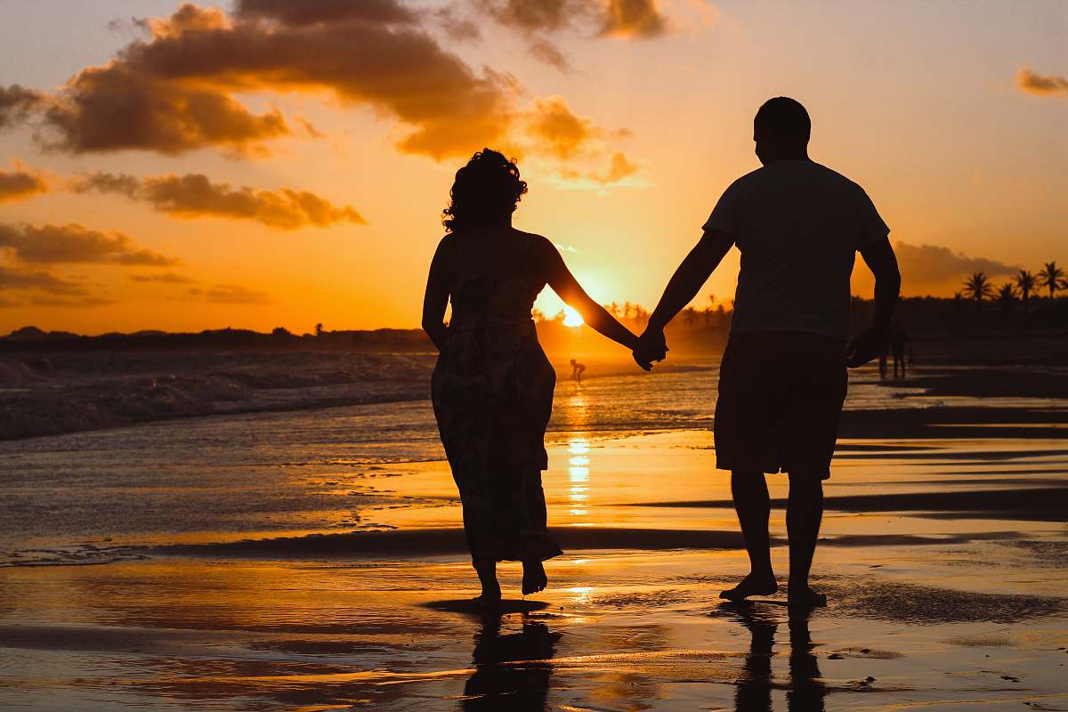 human couple standing on body of water during golden hour hand