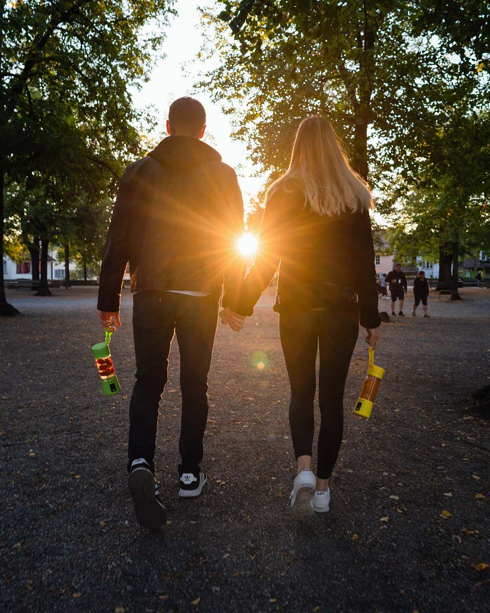 human man and woman in black jacket walking on pathway near trees apparel