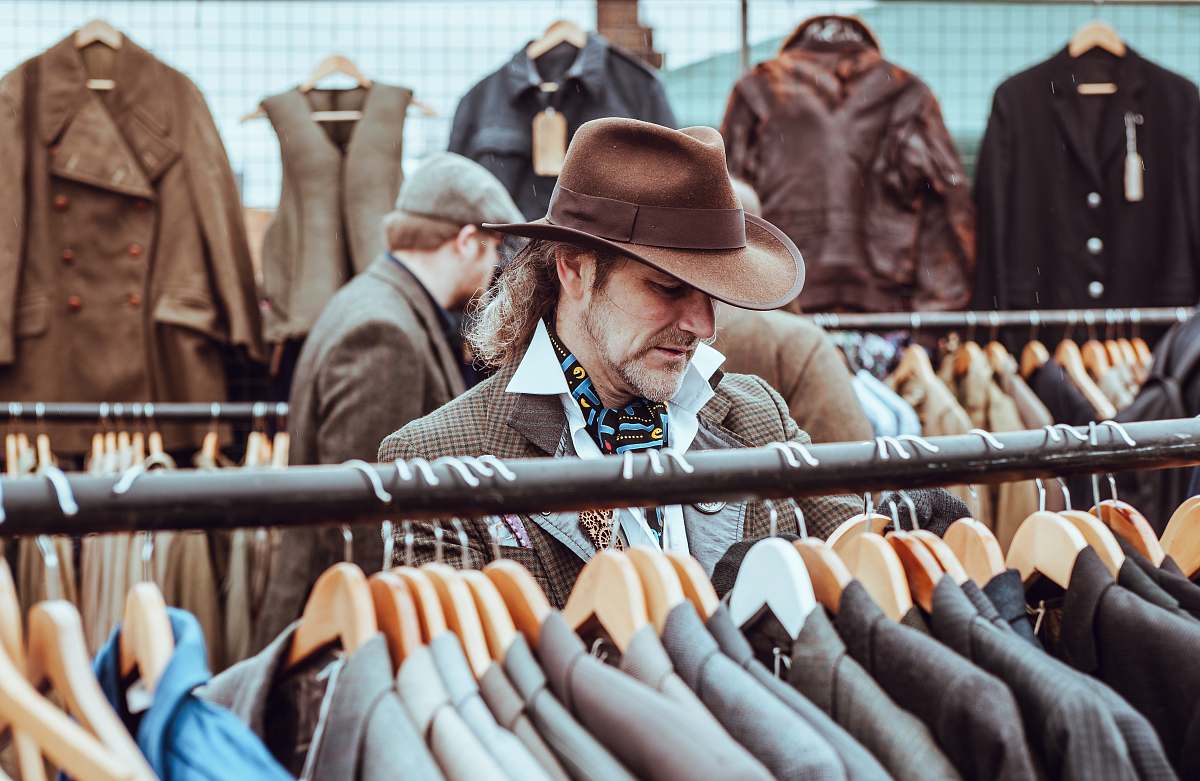 human man in brown cowboy hat in front of hanged suit jackets hat