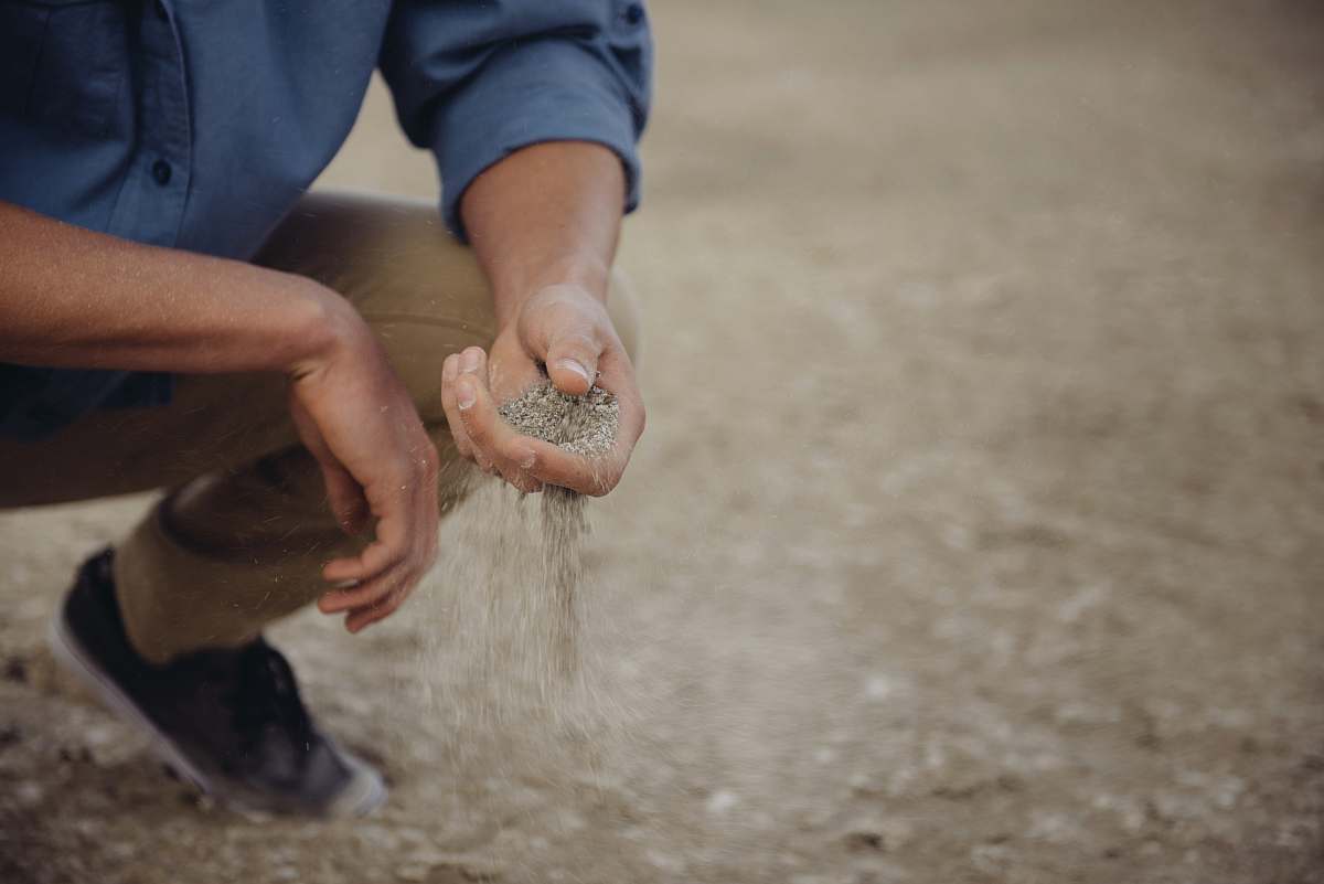 human Person crouches down with a handful of sand that slips through their fingers people