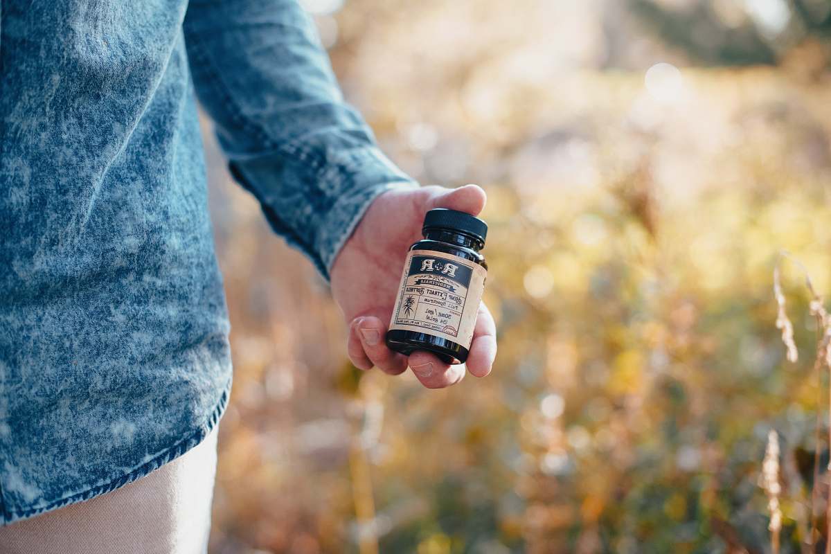 hemp person holding beige and black glass bottle human
