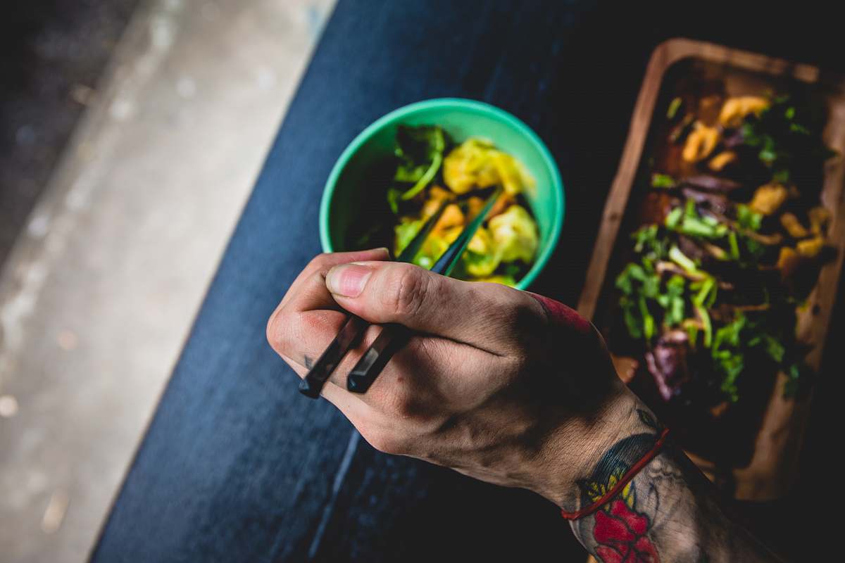 human person holding chopsticks near green bowl food