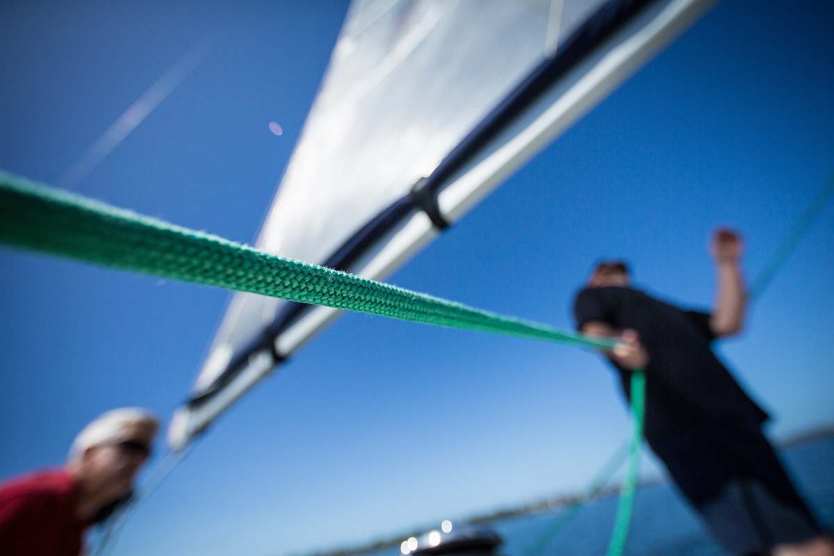 sailing person holding green rope near boat sail human
