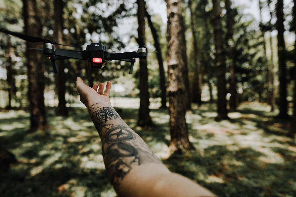 human person holding lack drone surrounded by trees skin