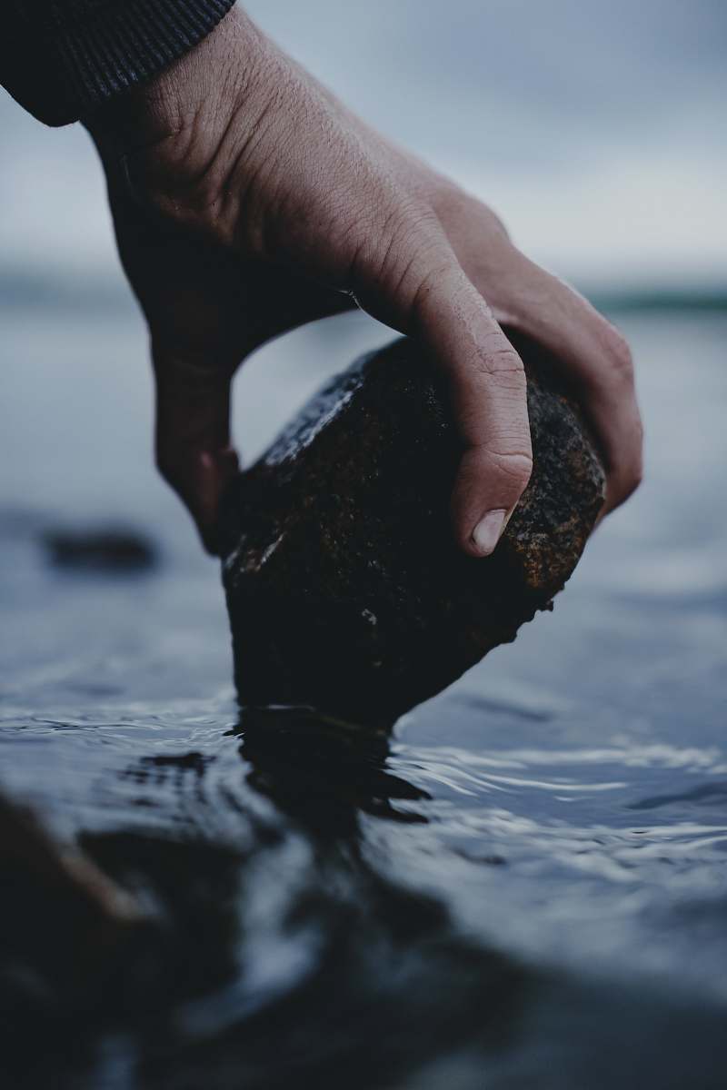 human person holding rock over water finger