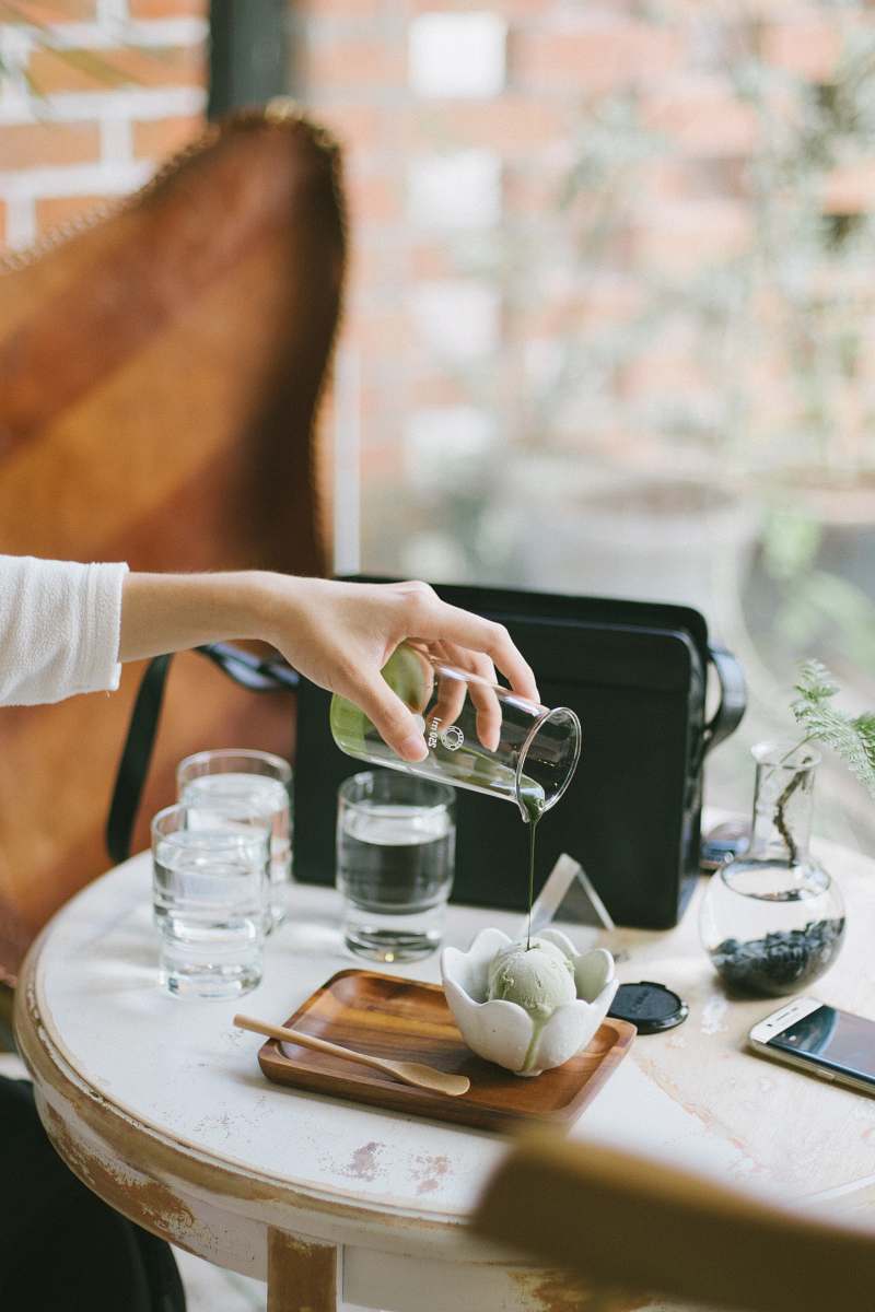 table person pouring green liquid on ice cream on scalloped-edge white ceramic bowl malaysia