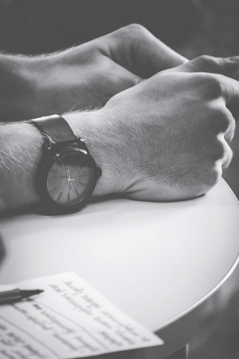 black-and-white person wearing black watch with hand on table wristwatch