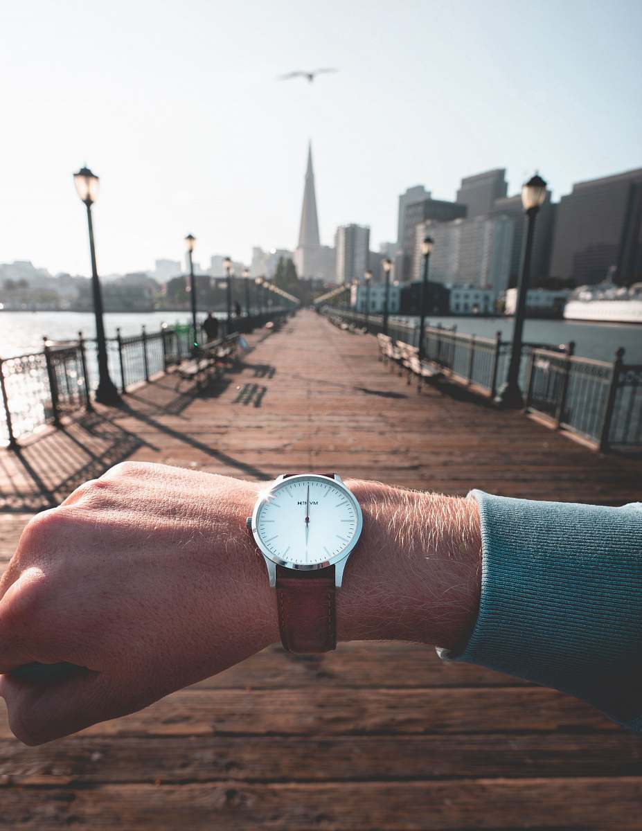 human person wearing round silver-colored analog watch with leather band displaying 12:00 time wristwatch