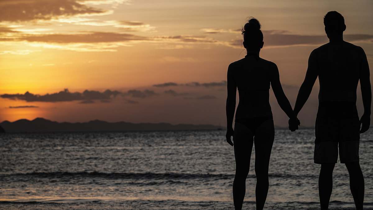 human silhouette photography of man and woman holding hands front of the sea standing