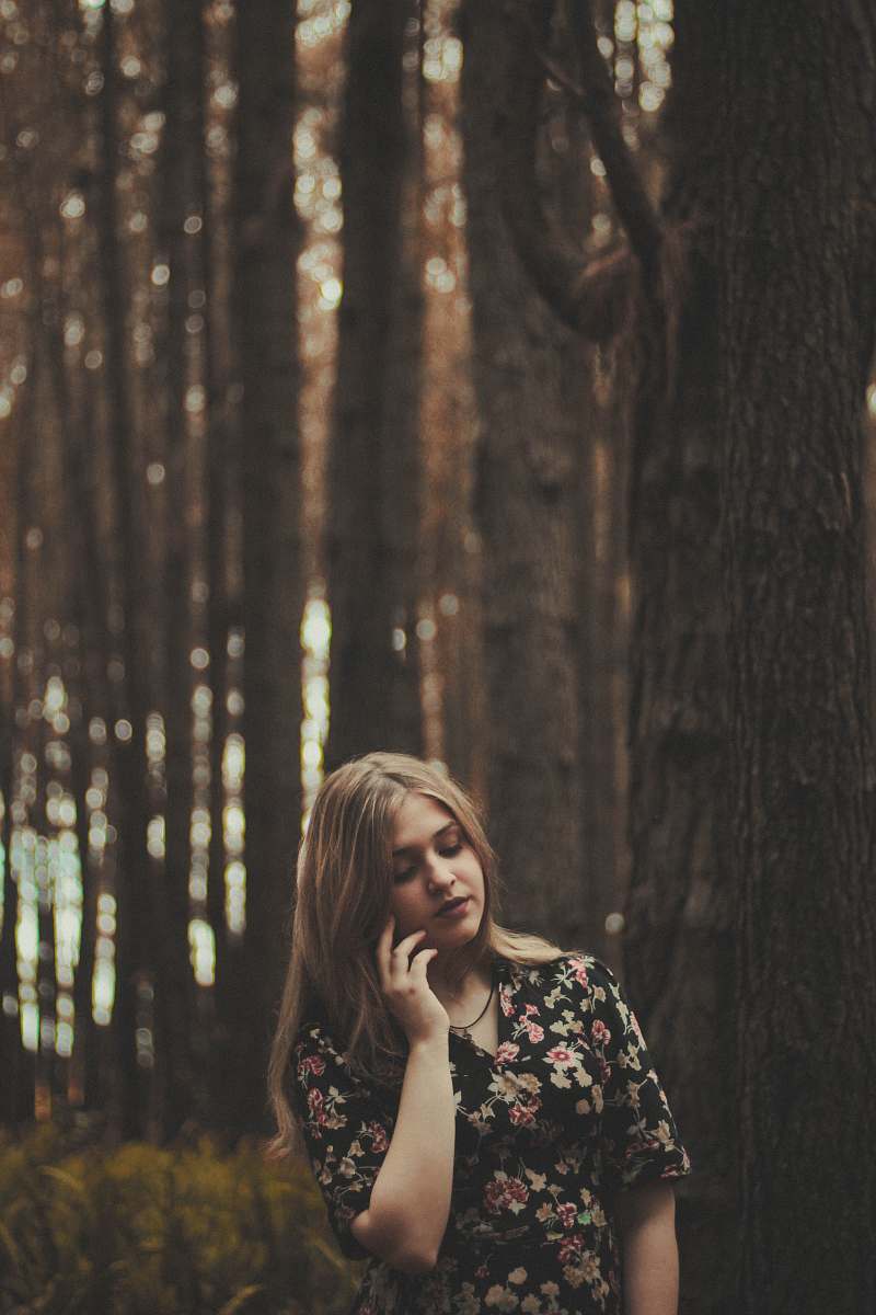 human standing woman beside gray tree while holding left cheek during daytime girl