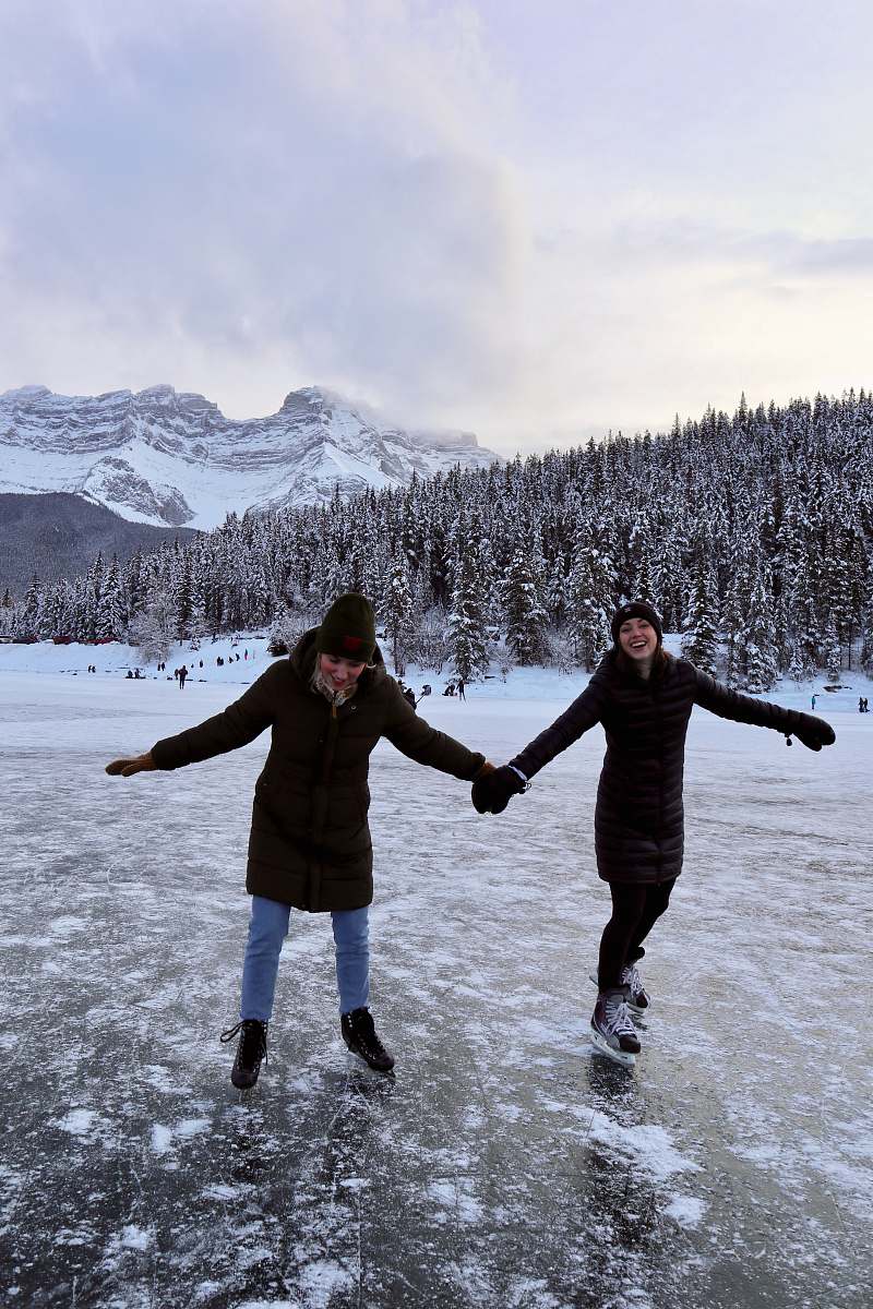 human two women standing on ice wearing skates and holding hands during day skating