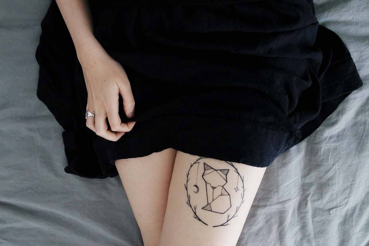 human woman lying on bed sowing cat dreamcatcher tattoo on right leg during daytime dress