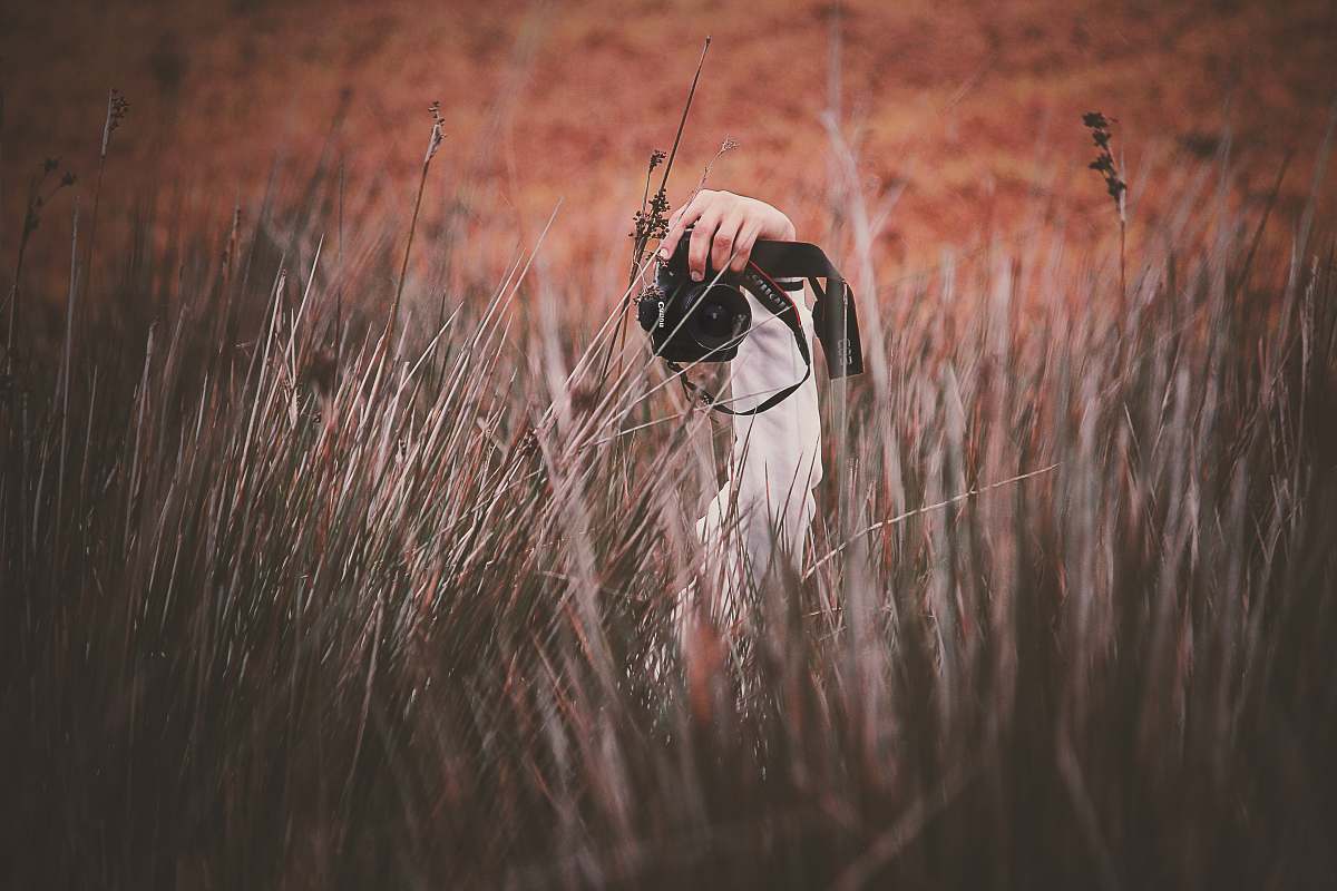 grass person holding Canon DSLR camera flora