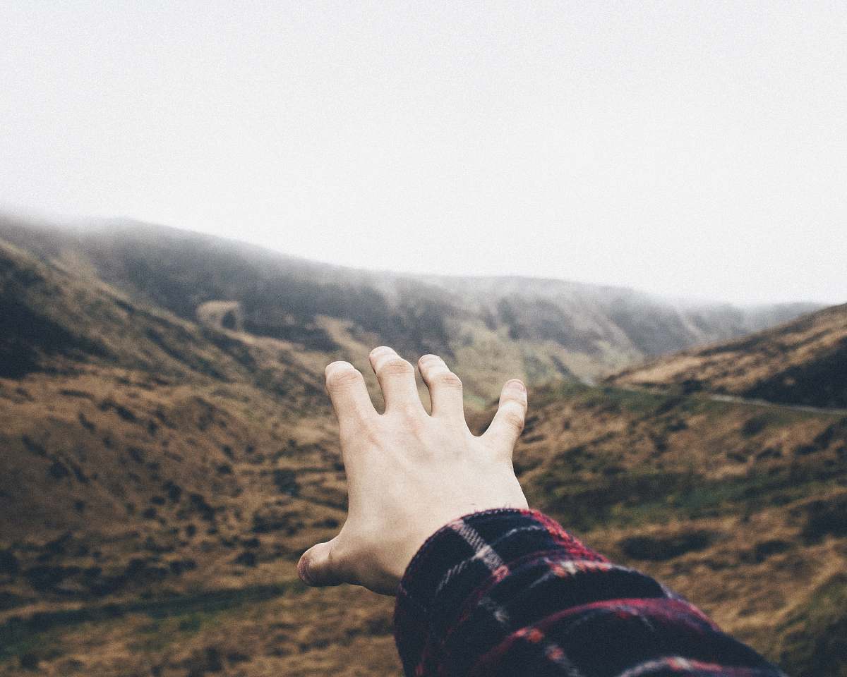 hill point of view photography of person raising hand towards mountains hillside