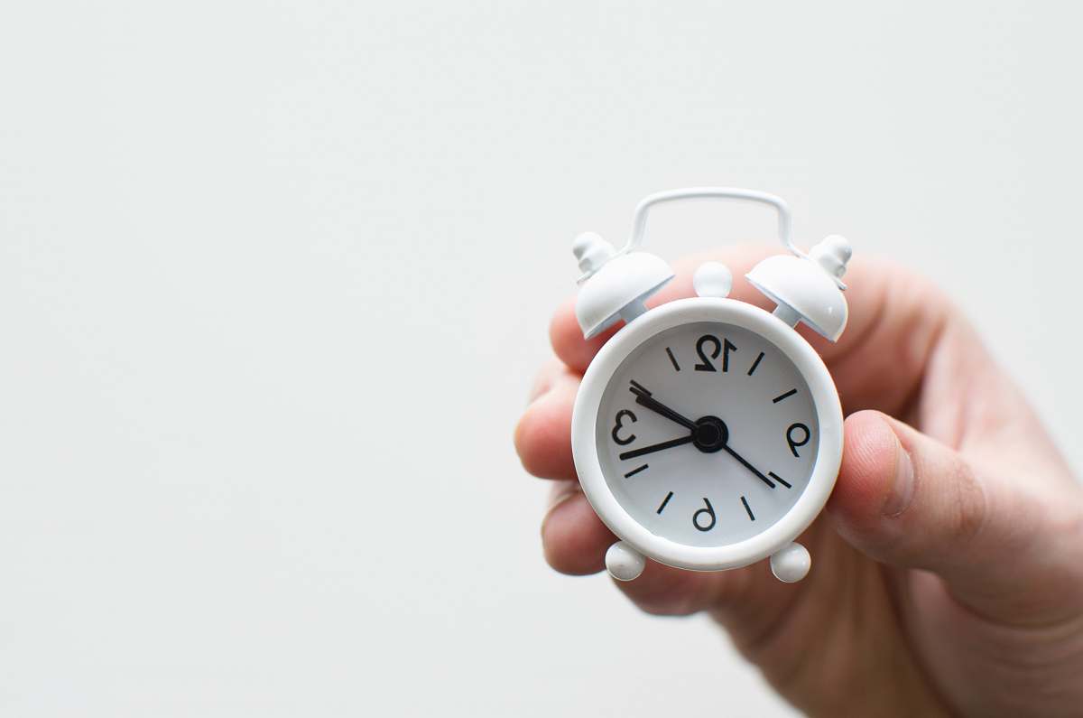 timepiece person holding white mini bell alarmclock holding