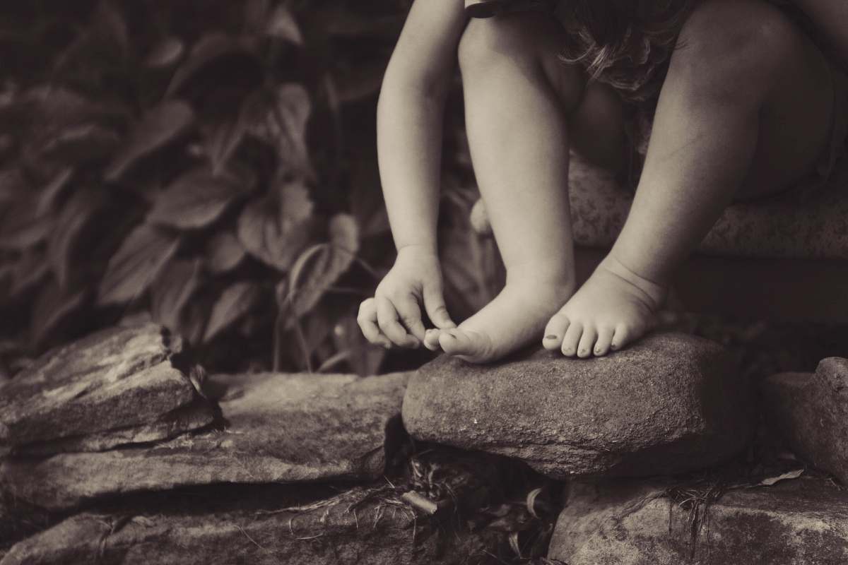 rocks depth photography of child sitting on rock beside plant kid