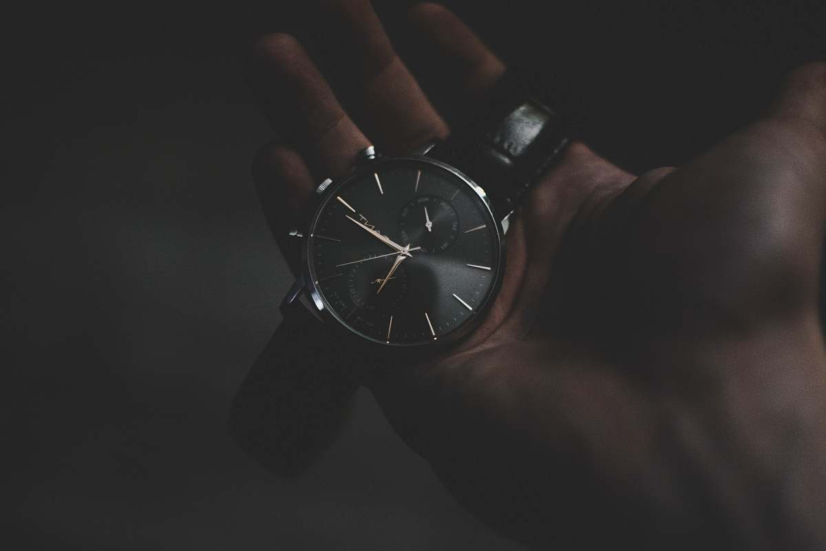 gold person holding watch pointing at 6:17 clock